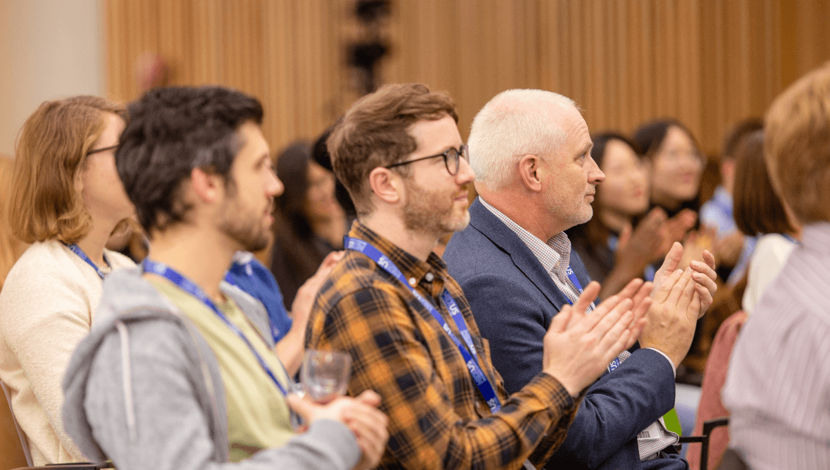 Three men in the foreground of a crowd applauding