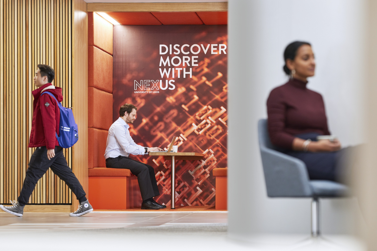 The Nexus atrium showing a student passing through, a man working in a booth and a woman at the front in a meeting
