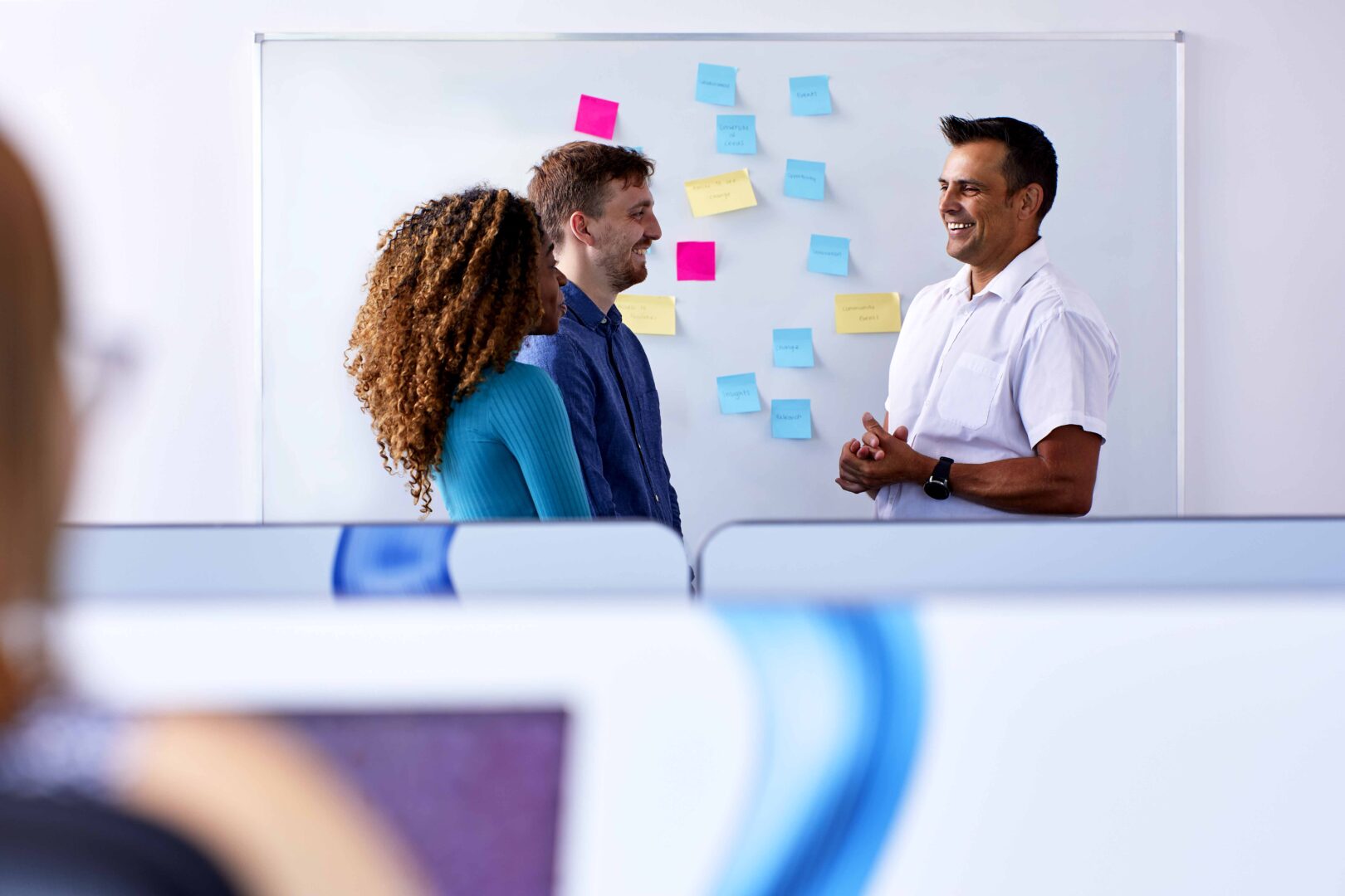 Three people stood in front of a whiteboard with post it notes on