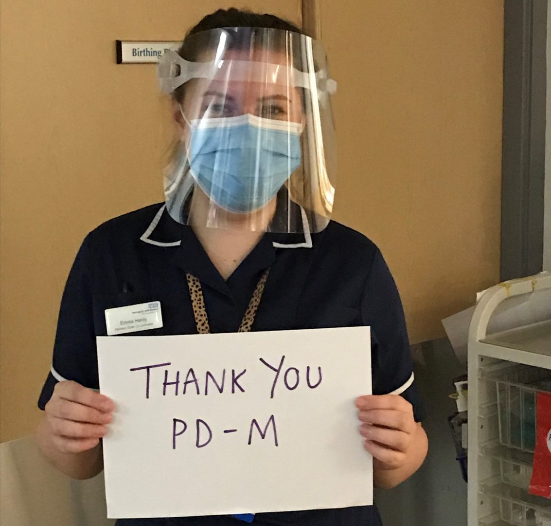 NHS nurse wearing face shield and mask holding up sign saying 'Thank you PD-M'