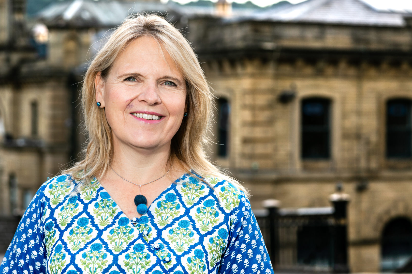 Head and shoulders shot of Kersten England, Chief Executive of Bradford Council. Kersten is stood facing camera and smiling with a building visible in the background.