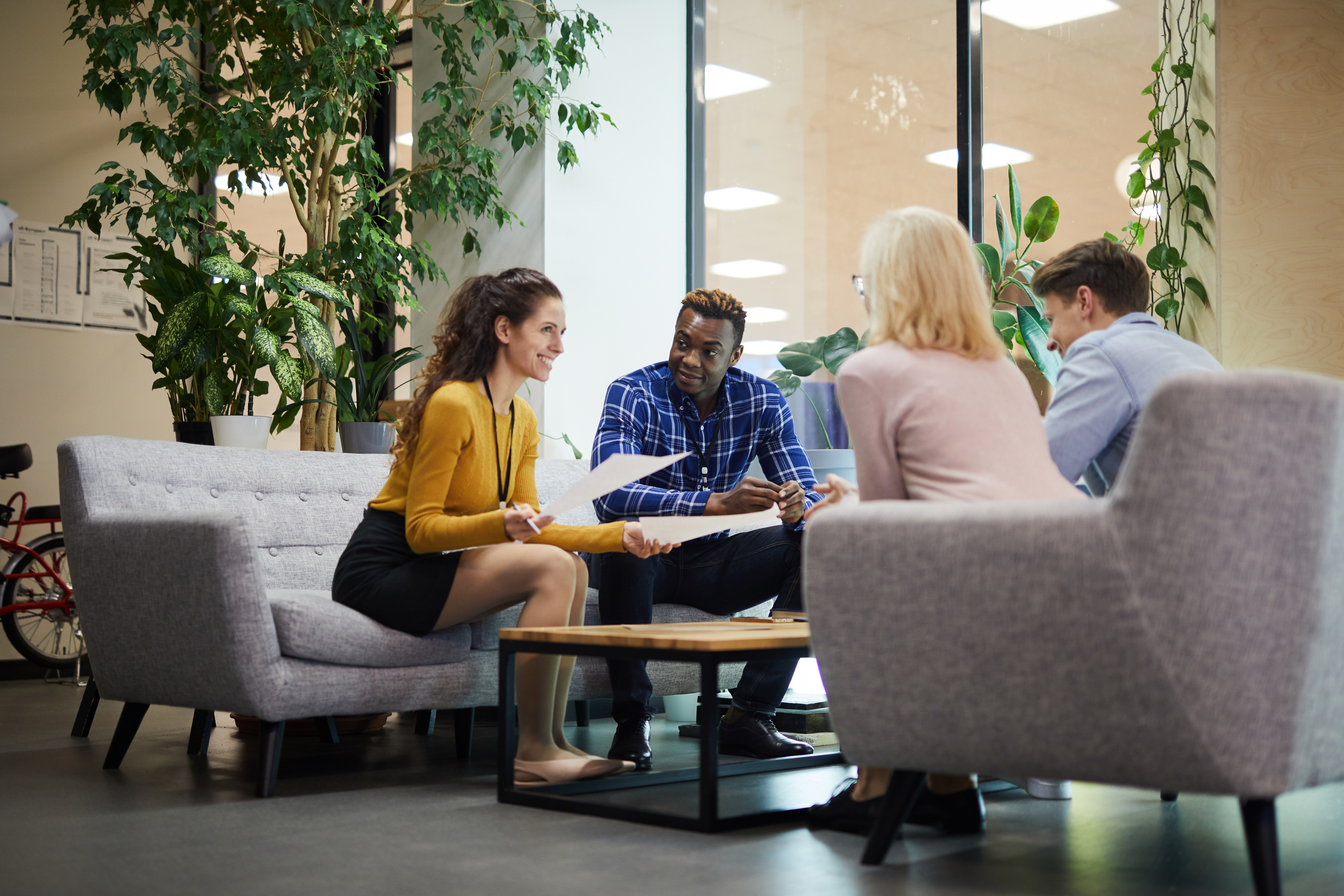 Group of four colleagues sat in casual lounge environment, conversing.