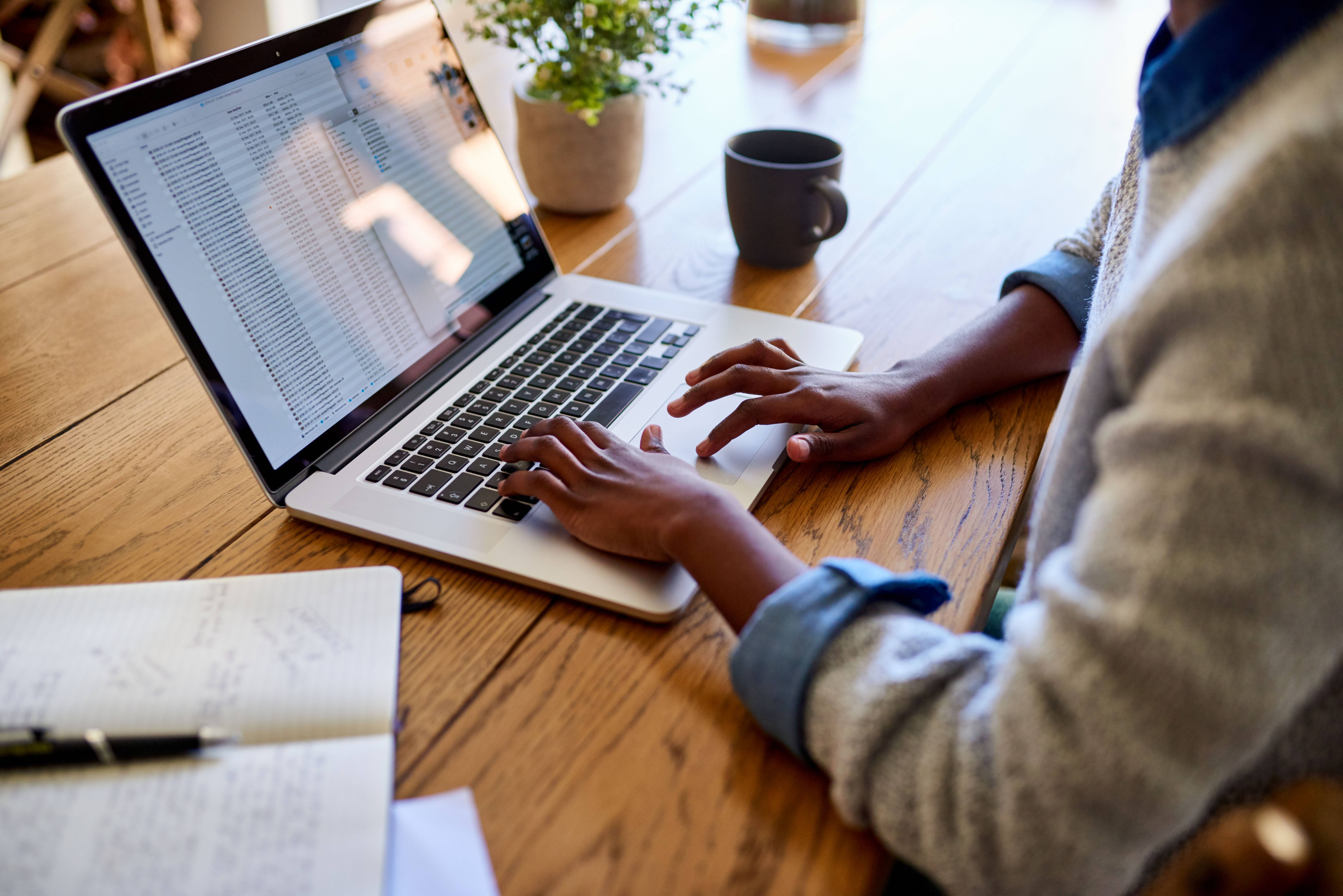Image of hands and arms of a person working on a laptop in a home environment