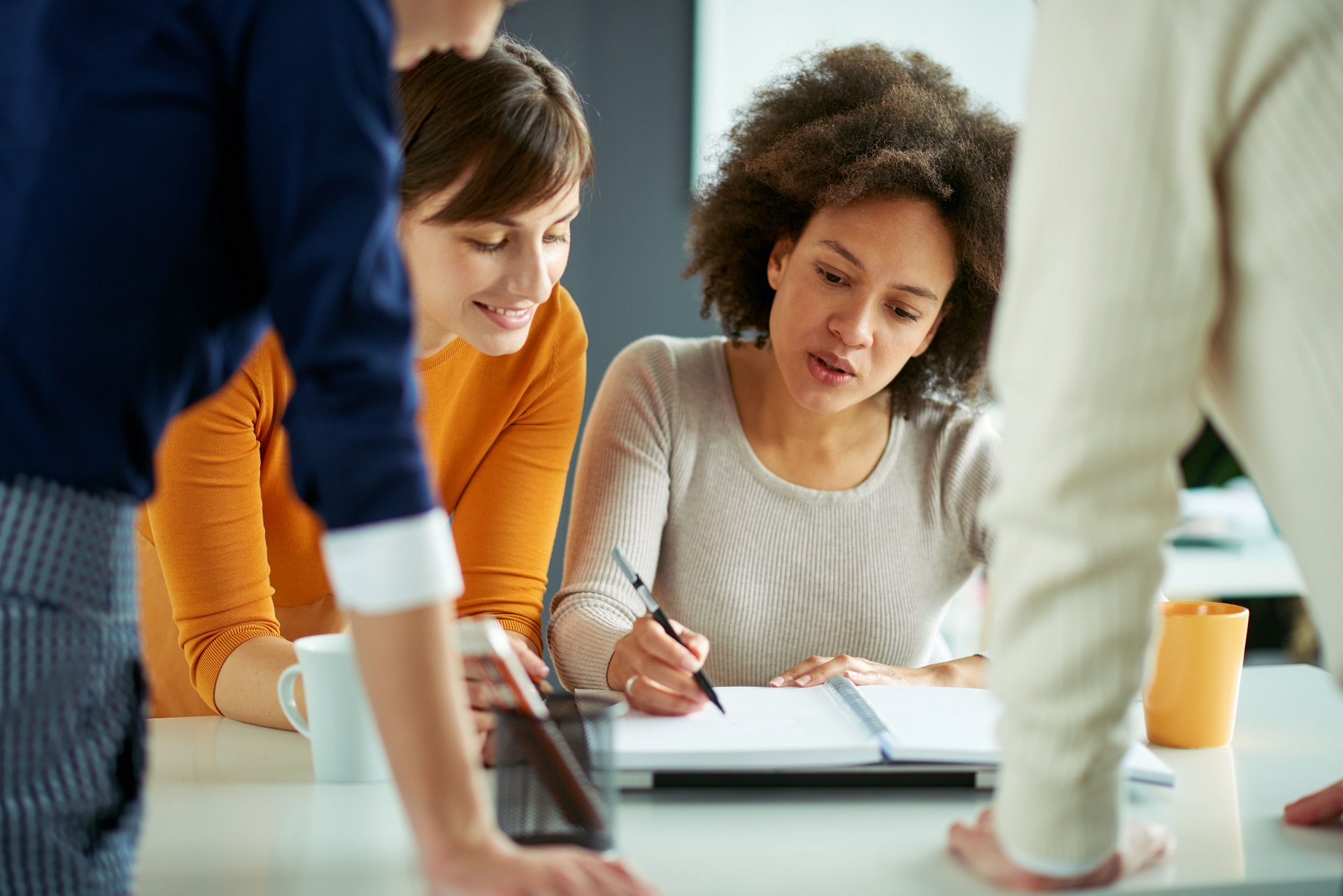 Woman sat at a table makes notes, surrounded by colleagues