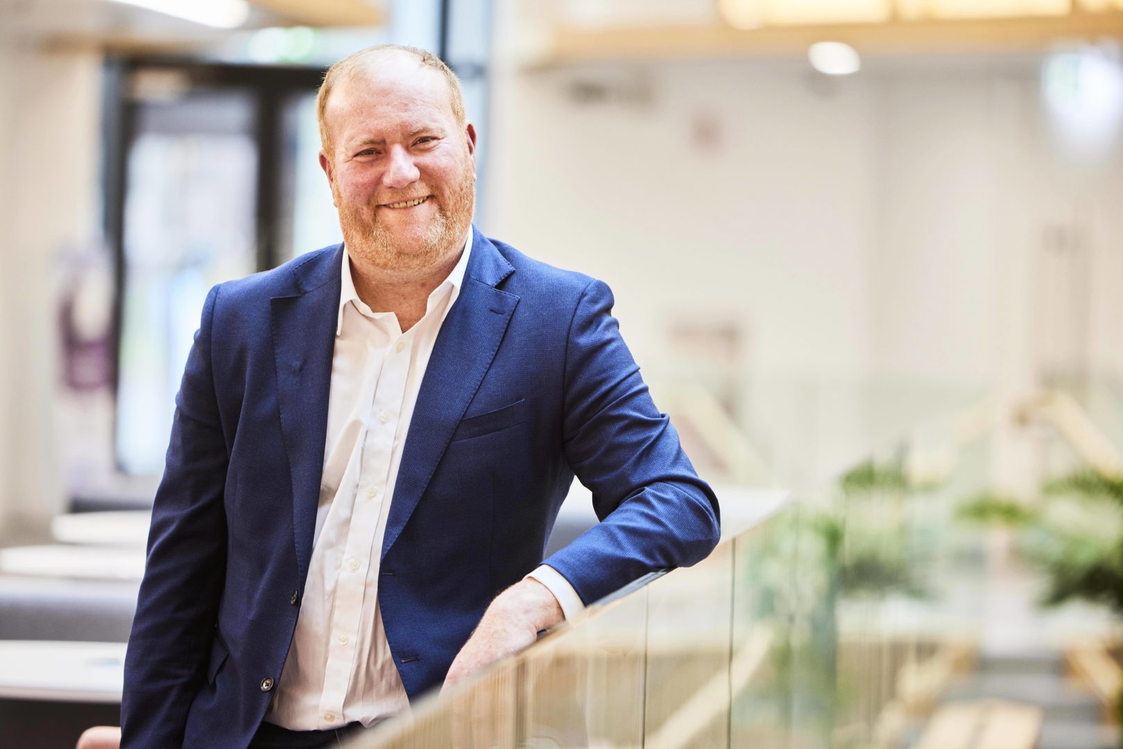 Image of Barry Singleton standing and leaning with his left arm on a glass balcony within the Nexus building. He is smiling to camera.