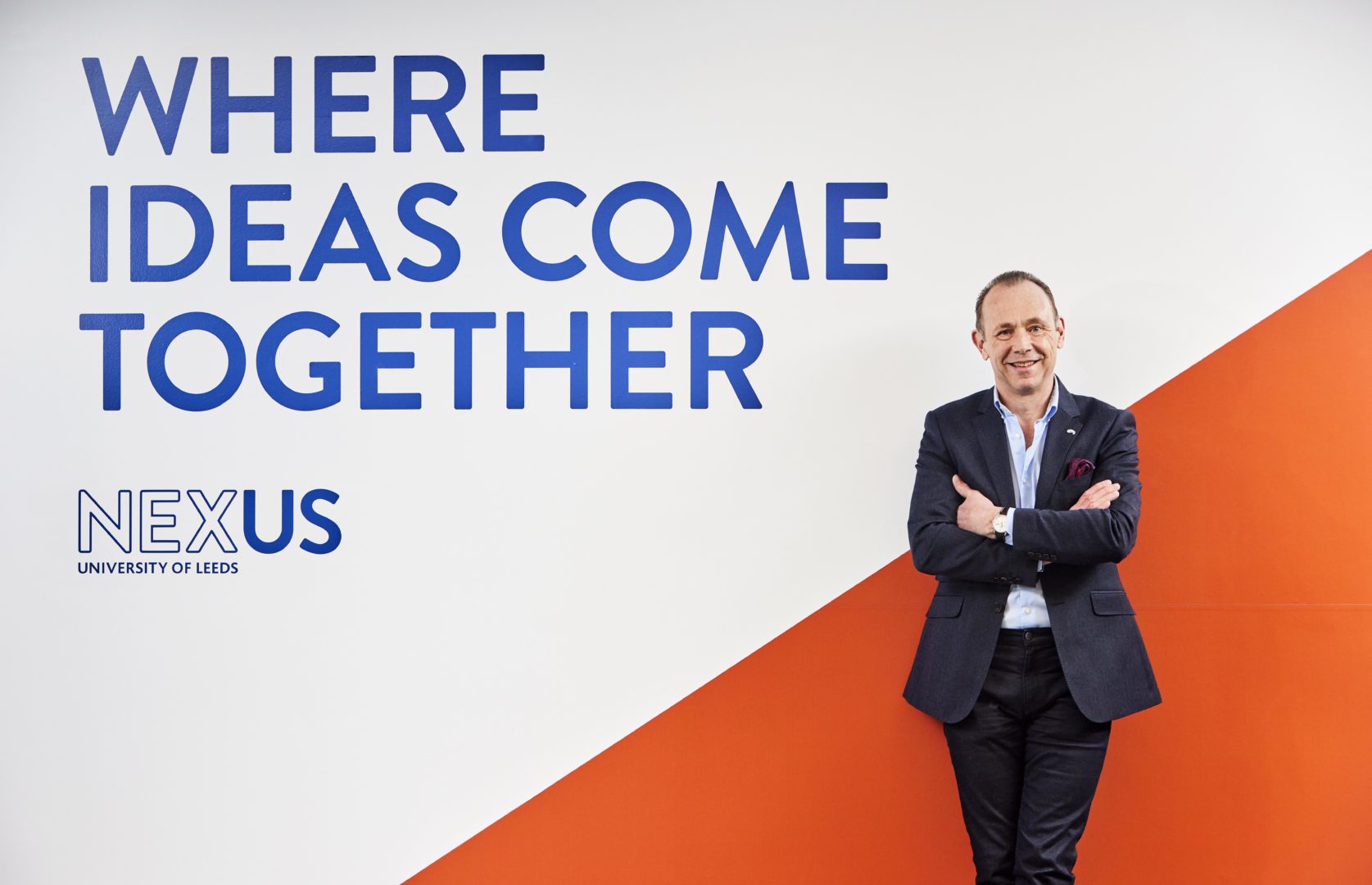 Dr Martin Stow, Nexus Director stood in a casual pose in front of a wall in the Nexus building. The wall reads where ideas come together.