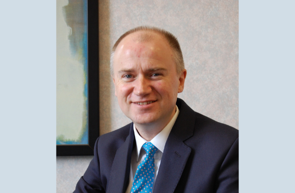 Head and shoulder portrait of Tom Riordan CBE smiling at the camera