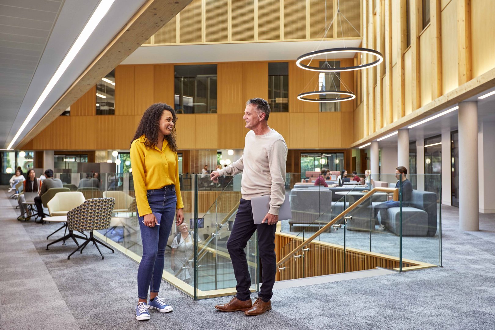 Two people having a conversation with people working behind them in the Nexus atrium