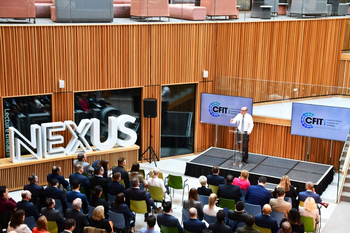 The Nexus atrium filled with an audience listening to a speaker on stage.